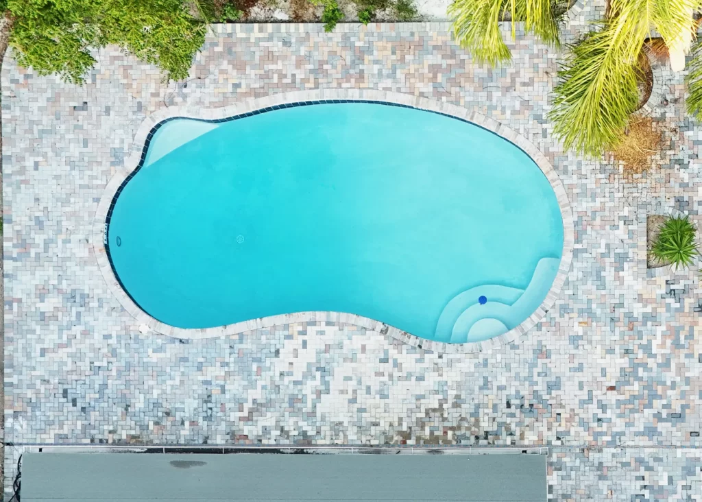 Overhead drone view of a freeform pool with paver deck and palms in Jacksonville, FL by Artegiano Contracting