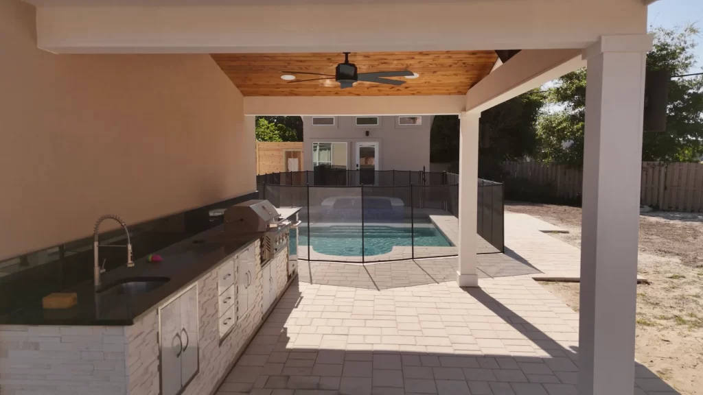 Covered outdoor kitchen with cedar ceiling, grill and granite counters overlooking a pool and spa in Jacksonville, FL
